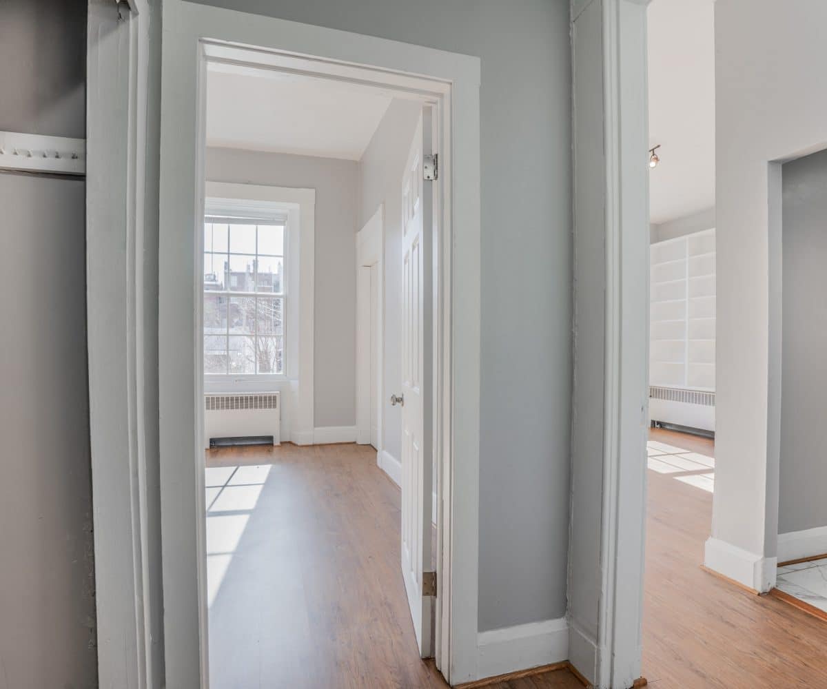 Hallway leading into sunny bedroom and living room with bookshelves.
