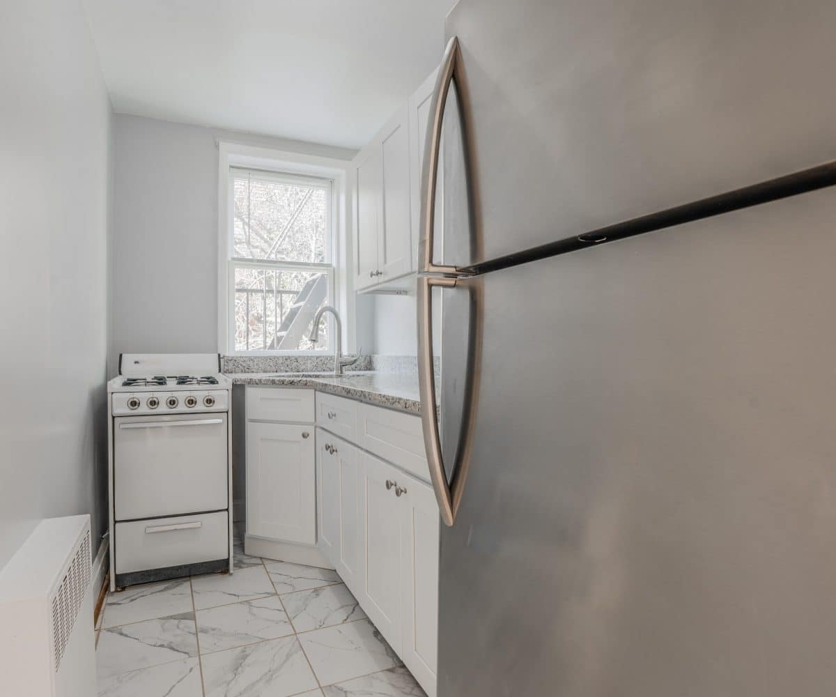 Small kitchen with granite countertop, white oven and stainless steel refrigerator.