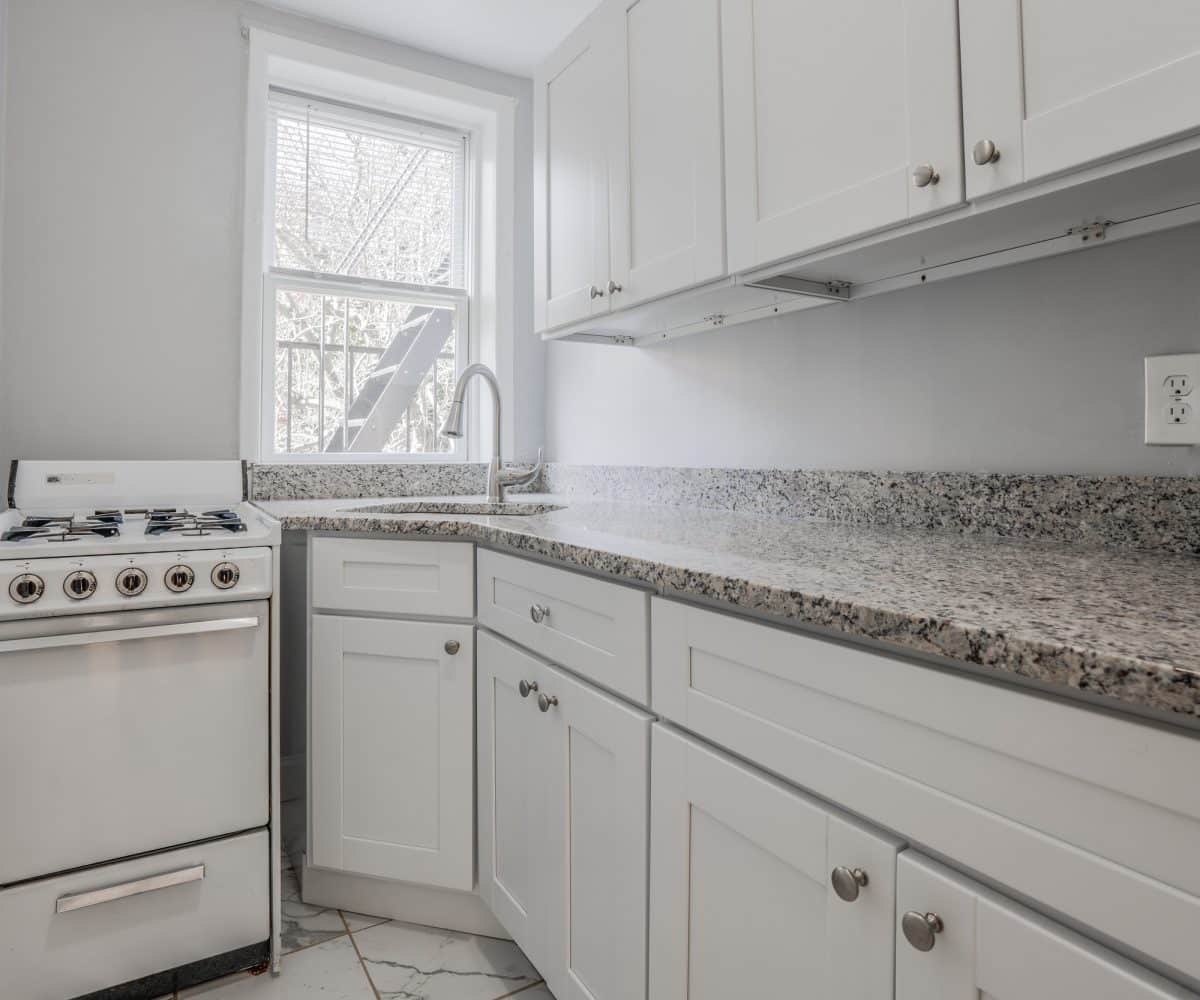 Kitchen with a long granite countertop, stainless steel sink and white oven.