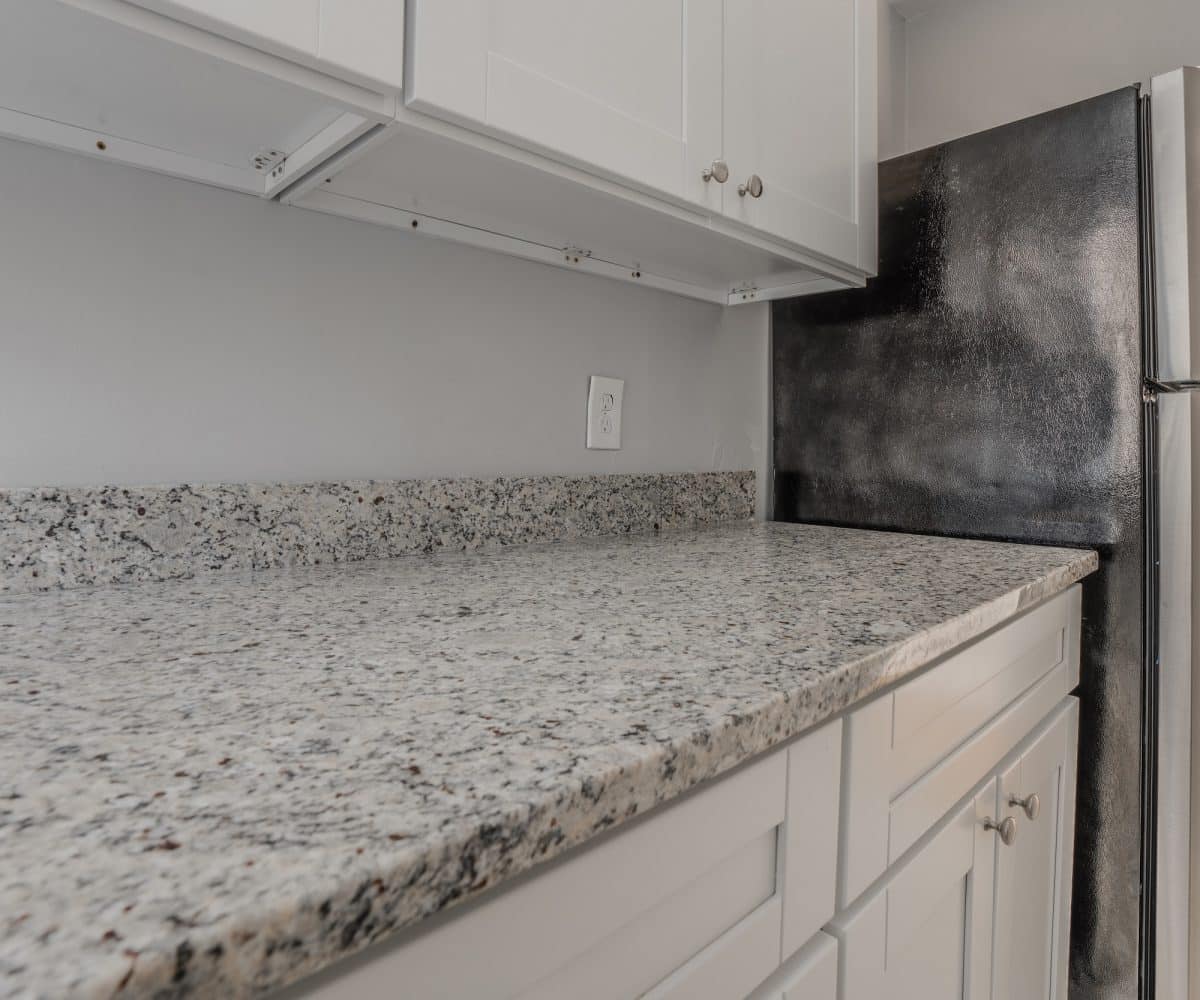 Granite kitchen countertop with white cabinets and a black refrigerator.