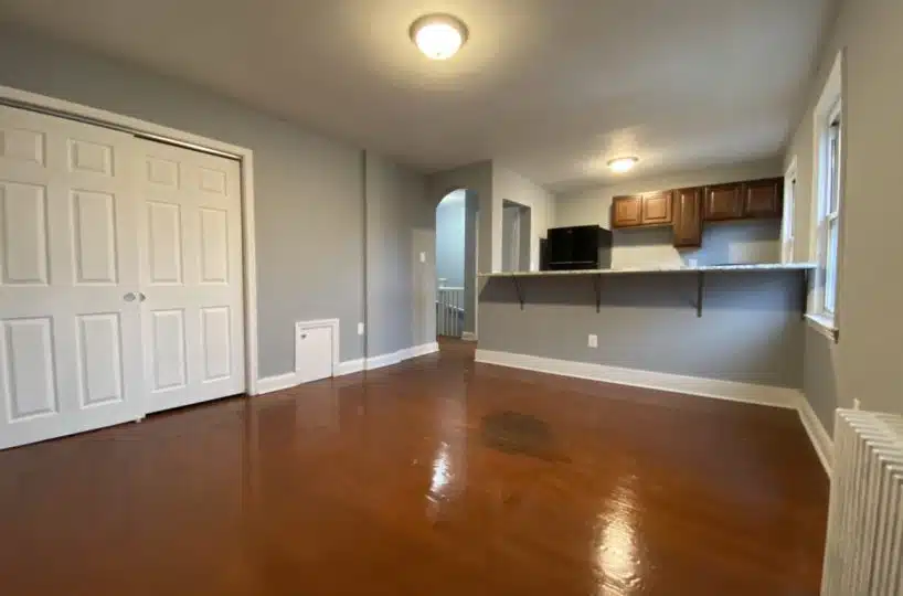 Grey colored living with red hardwood floors, kitchen island, fridge and wood cabinets.