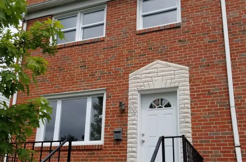 Red brick home with living room window and white front door.