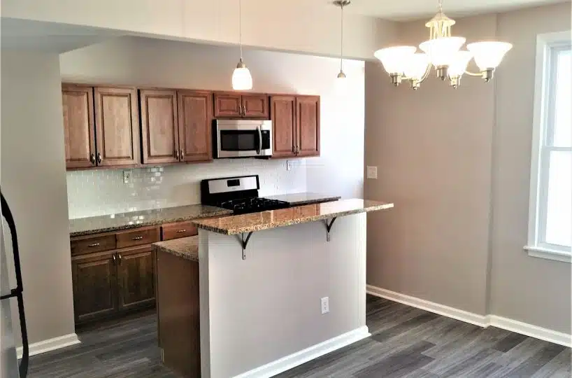 Open plan layout kitchen with marble counters, stove, microwave and wood cabinets.