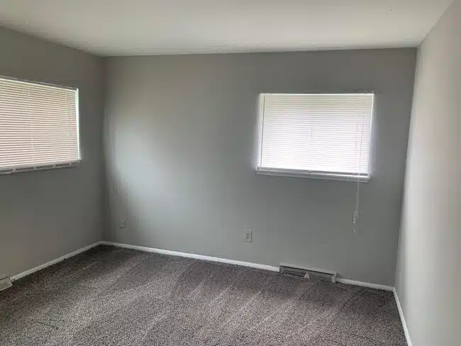 Bedroom with grey carpet, two windows and grey walls.