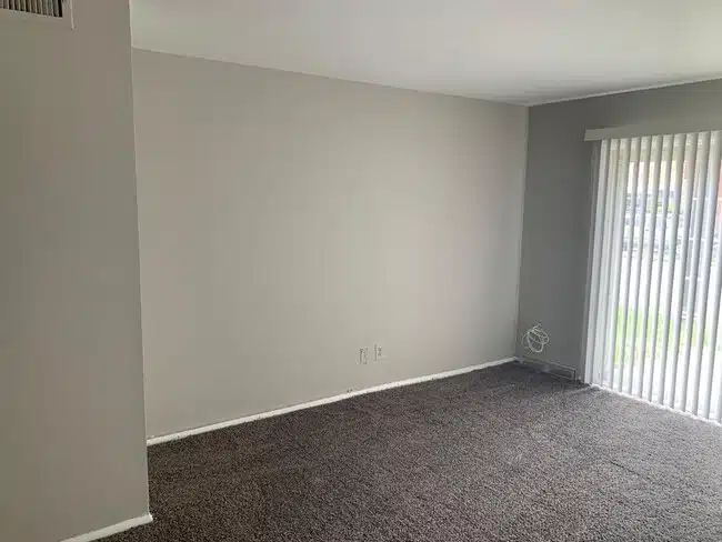 Carpeted living room with large window and white blinds.
