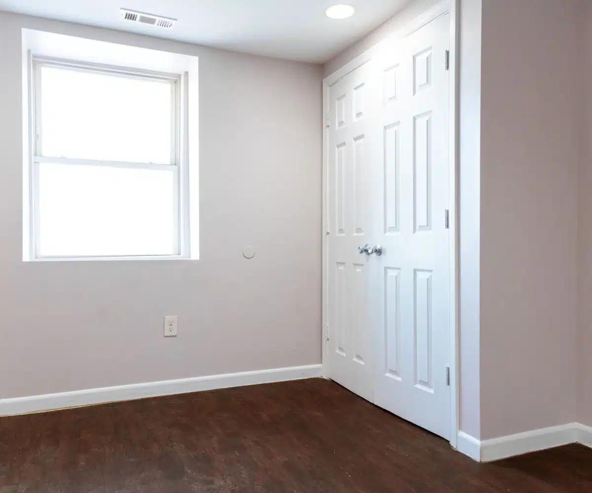 Bedroom with closet doors, window and hardwood floors.