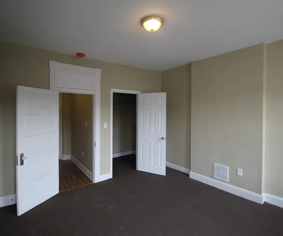 Carpeted bedroom with beige walls, white doors and closet.