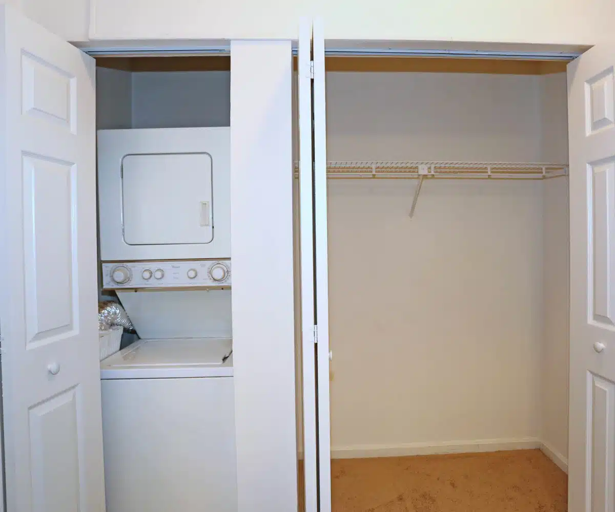 View of washer/dryer unit and carpeted walk-in closet with wire shelf.