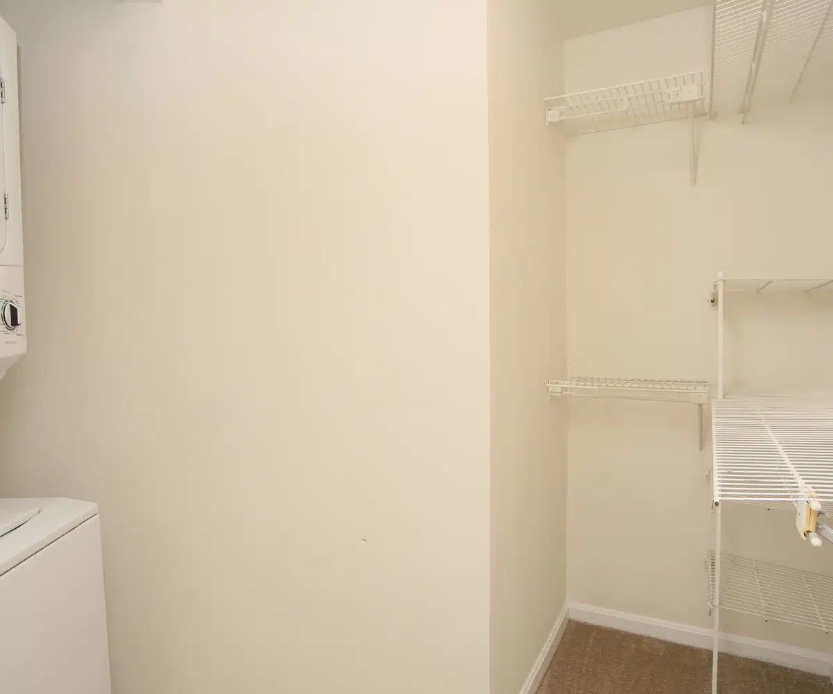 Carpeted laundry room with washing machine, dryer and wire shelves.
