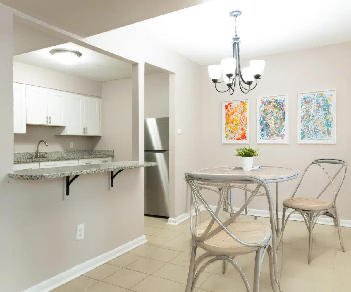 Kitchen with granite counters and stainless steel fridge and dining room with round table and two chairs.