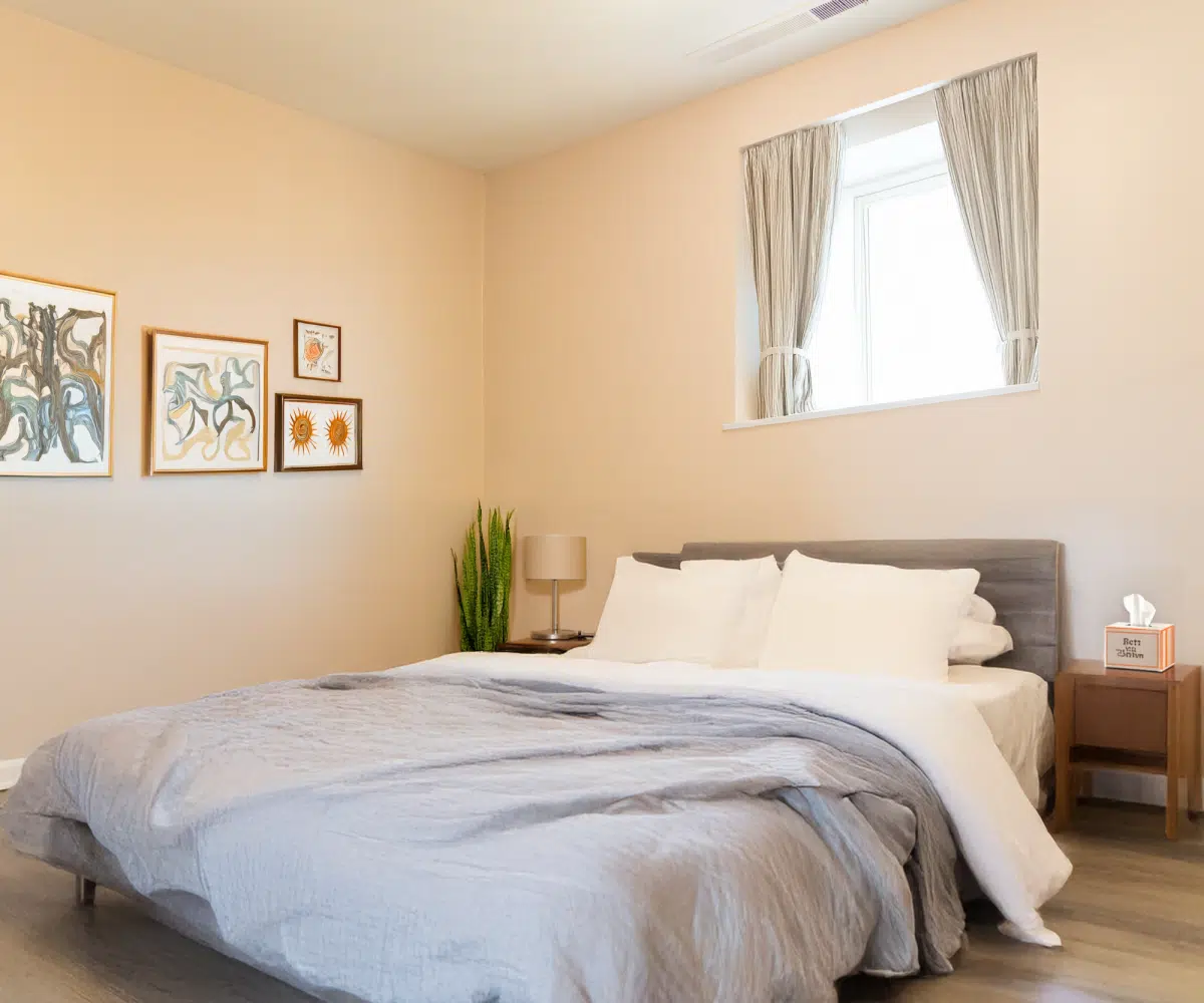 Beige bedroom with double bed, window and mirror.