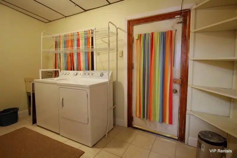 Laundry room with yellow floors, white door, red rug and washer and dryer.