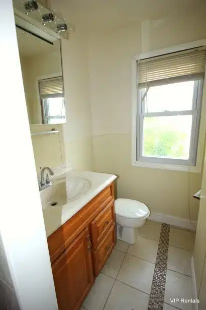 Bathroom with window, beige floor tiles, white scalloped sink and red cabinet.