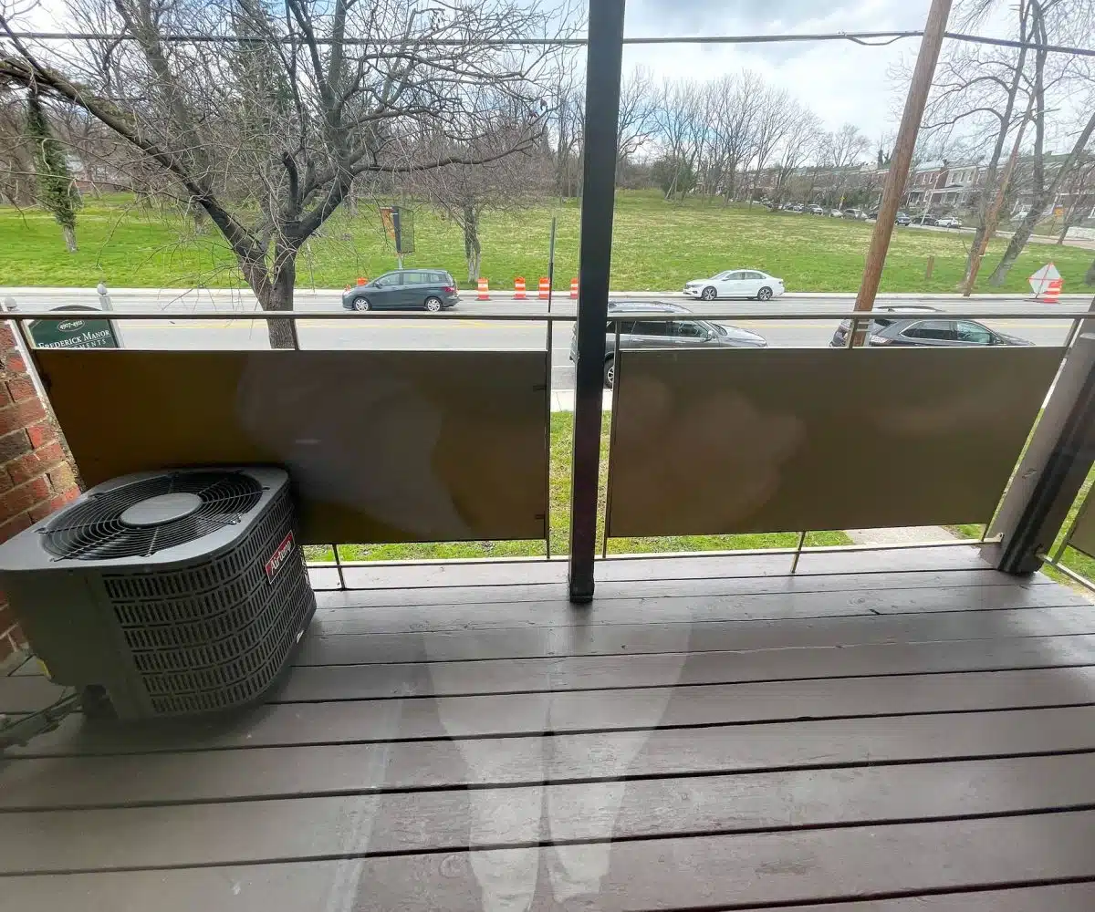 A balcony with a view of the street below with parked cars, trees and green grass.