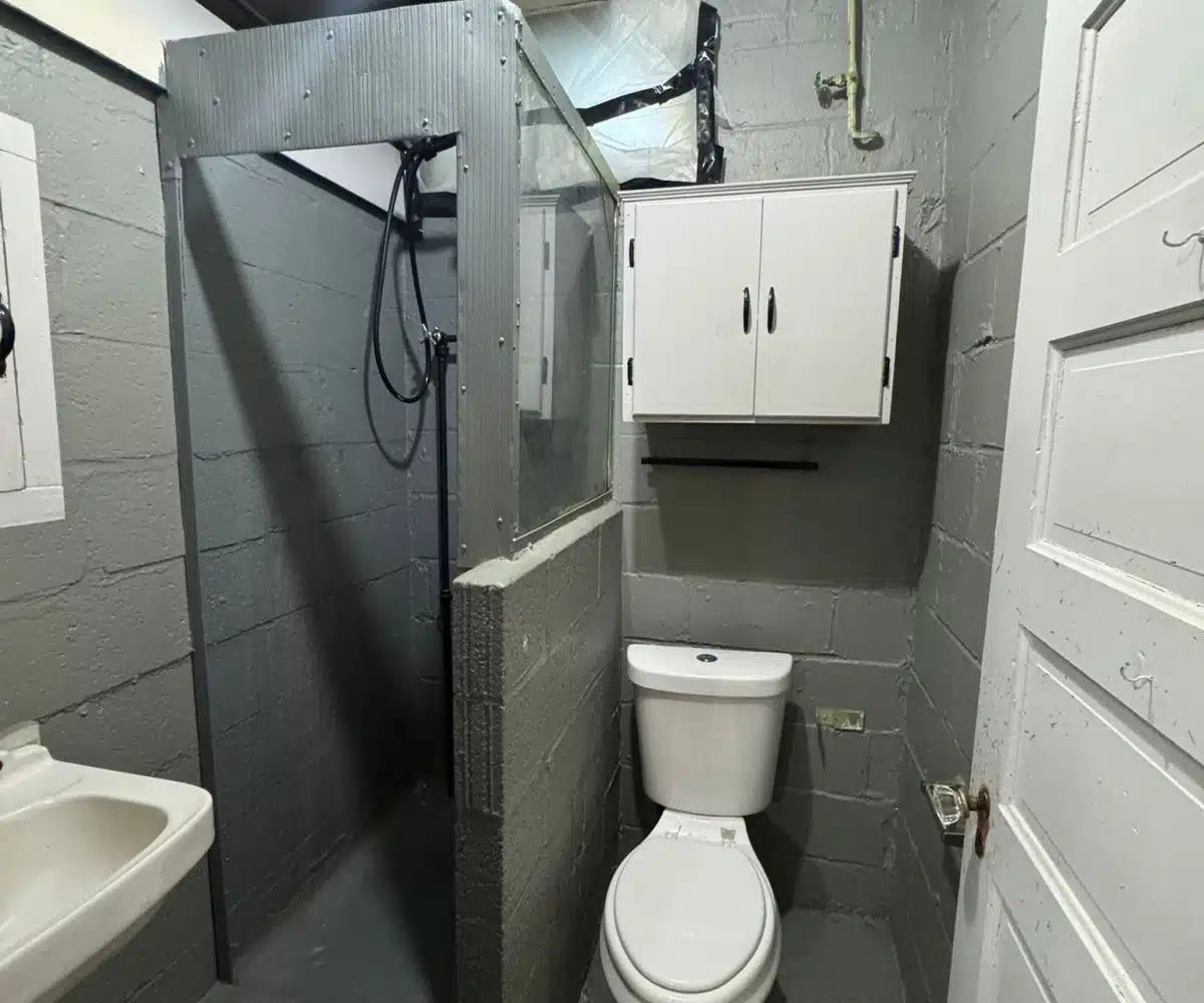 Bathroom with grey brick walls, a shower stall, a sink and a toilet.