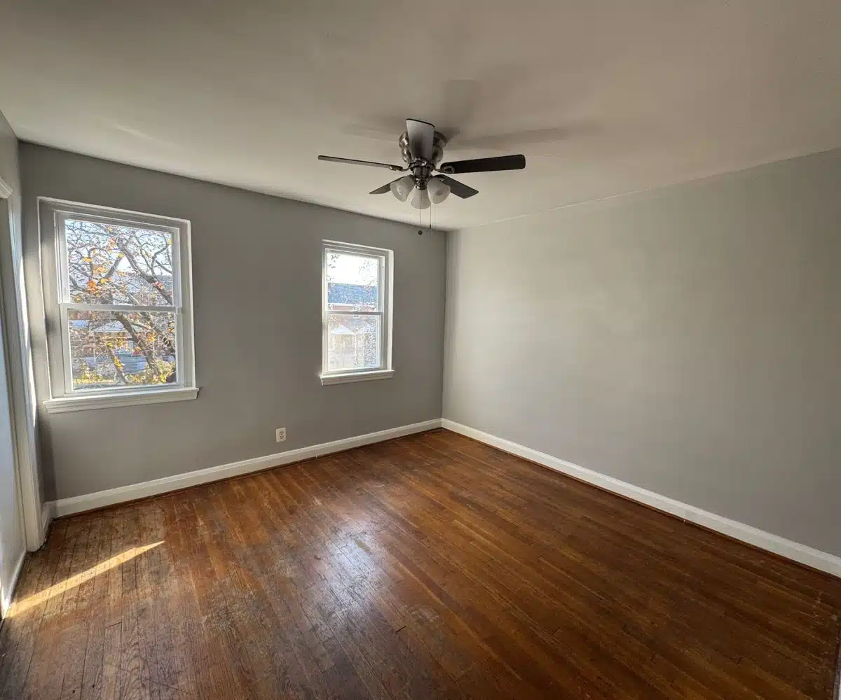 Bedroom with hardwood floors, ceiling fan and two windows.