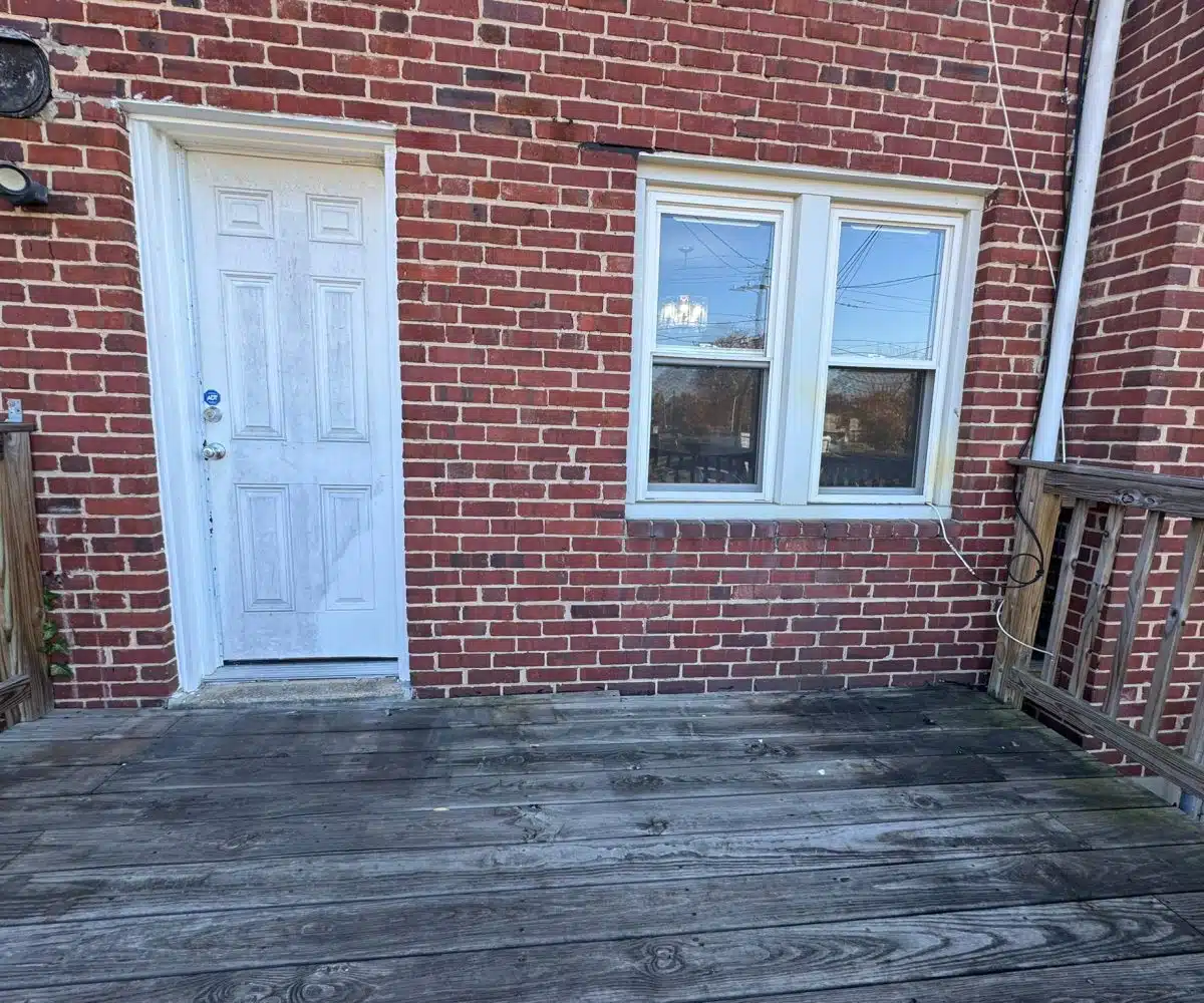 Red brick townhome with white door and wooden back porch.