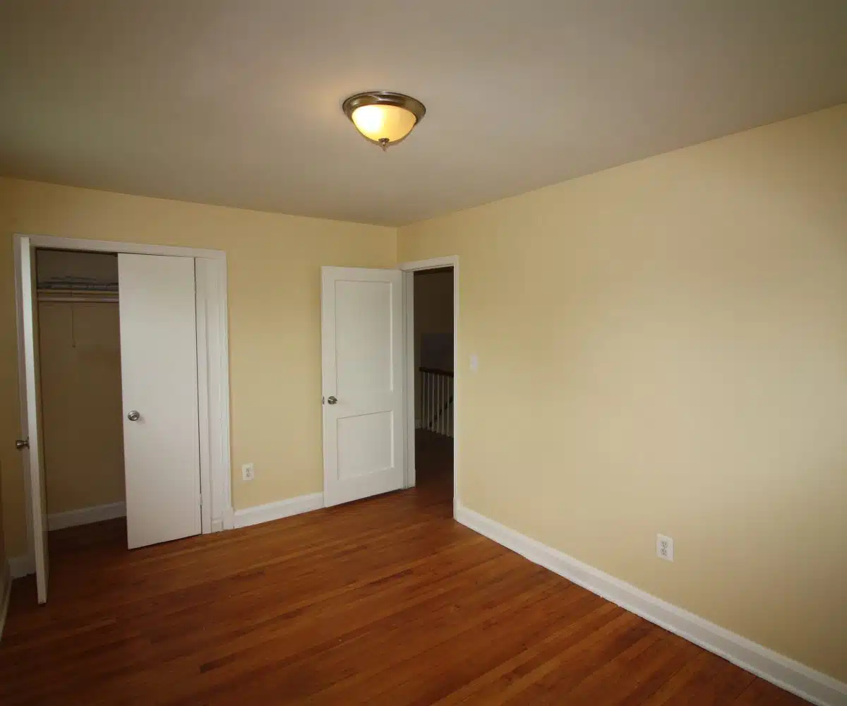 Bedroom with hardwood floors, yellow walls, large closet and ceiling light.