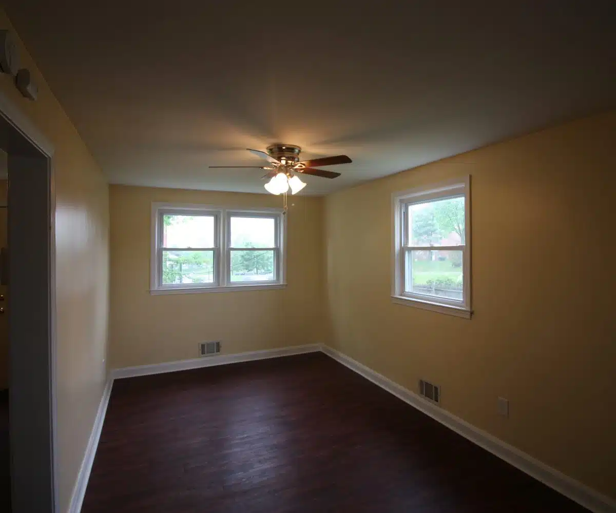 Dining room with hardwood flooring, ceiling fan with lights and three windows.