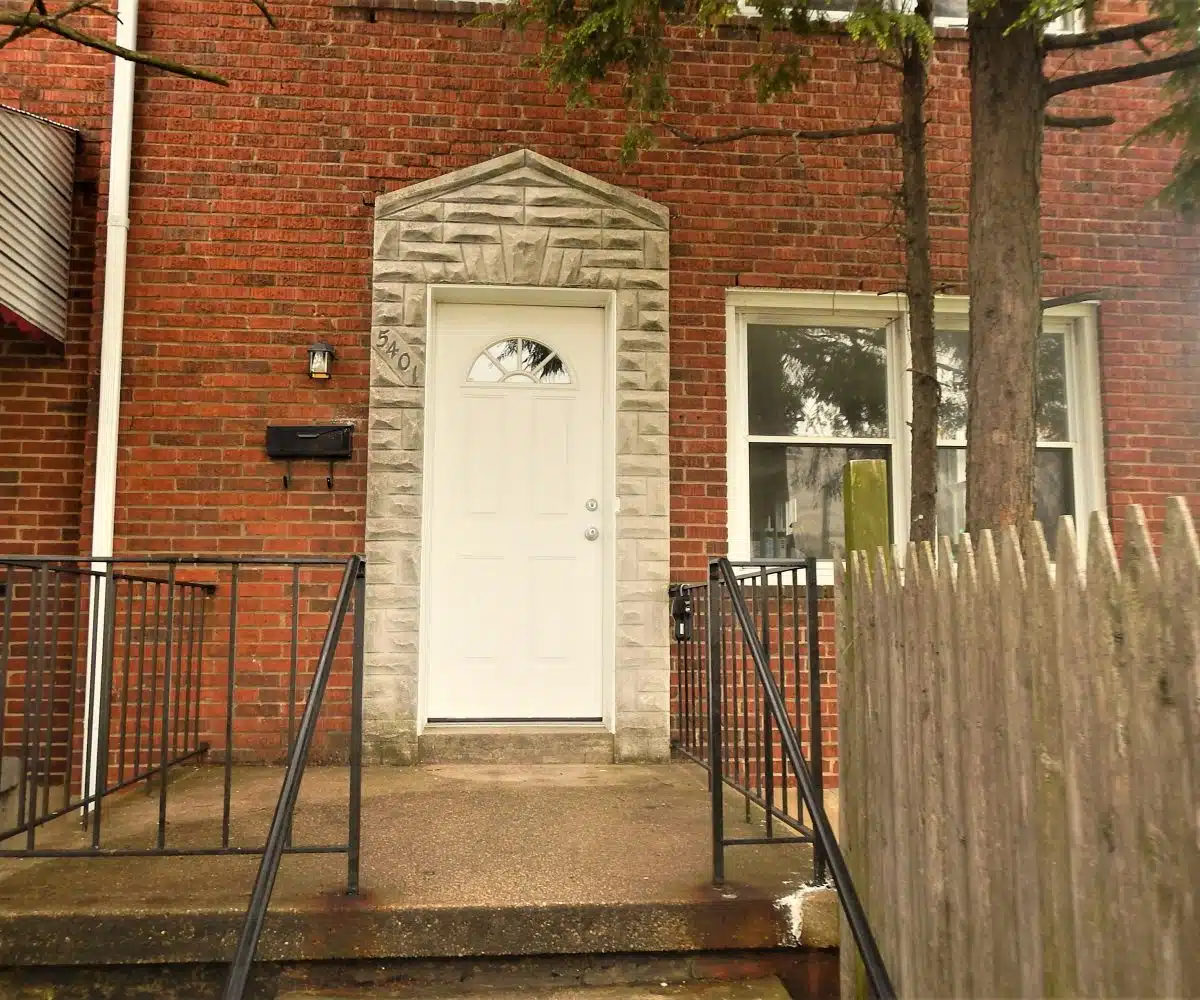 Redbrick townhome exterior with decorative white front door and concrete front porch.
