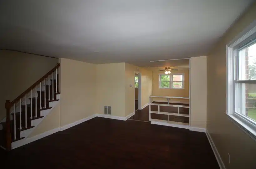 Living room with hardwood floors, yellow walls, a window and a staircase leading to the upper floor.