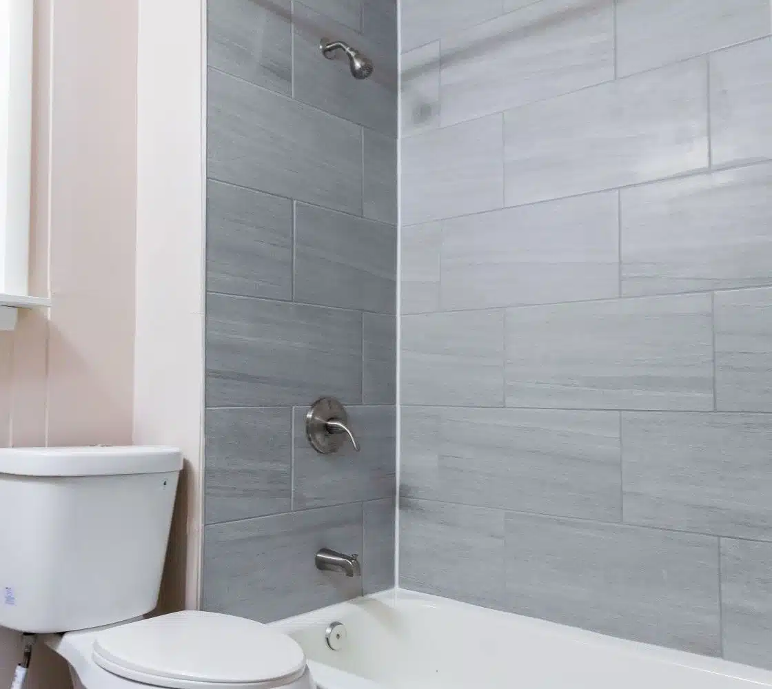Bathroom with grey tiled wall, bathtub and toilet.