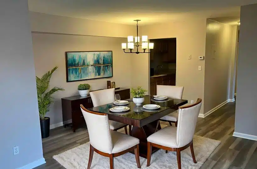 Dining room with white chairs, brown table, brown sideboard, blue picture and hanging light fixture.