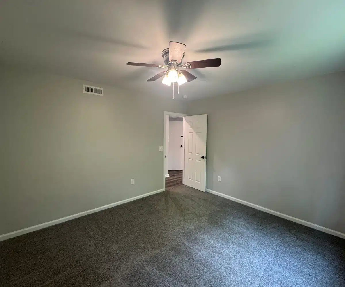 Bedroom with grey carpet and ceiling fan with three lights.