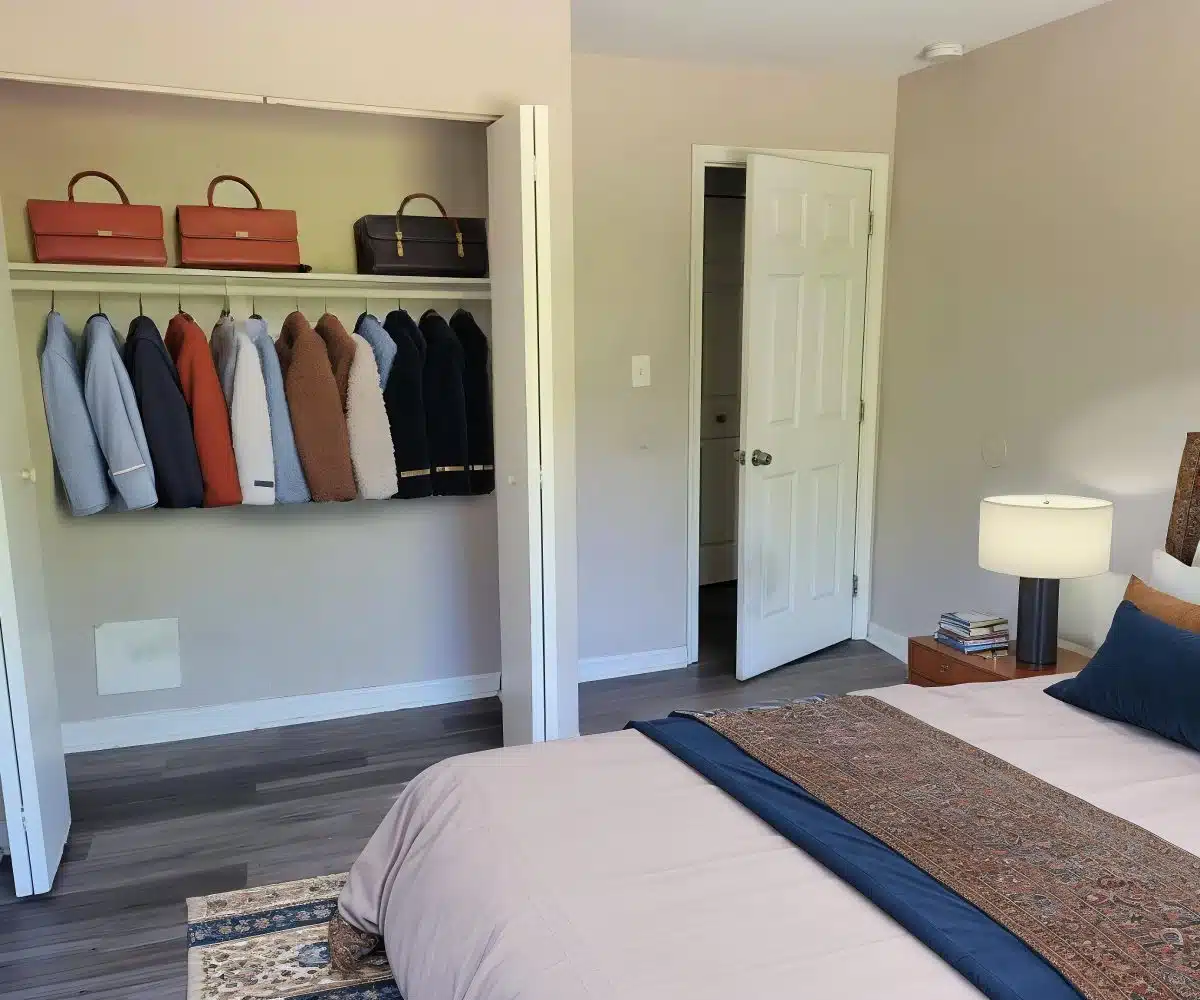 Bedroom with large closet, bed, table lamp and grey flooring.
