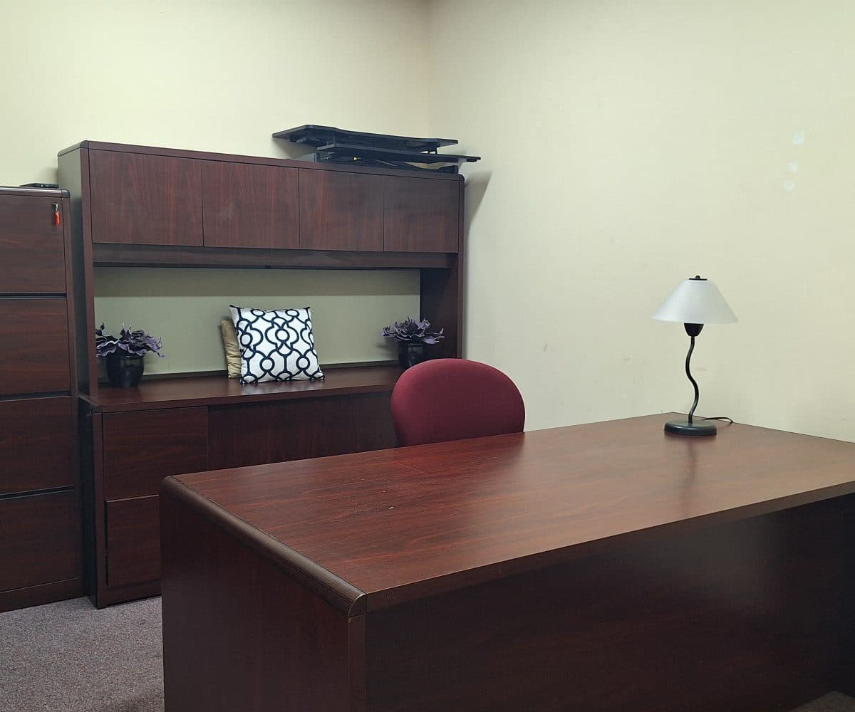 Office with wood desk, chair, lamp, wood shelves and carpeting.